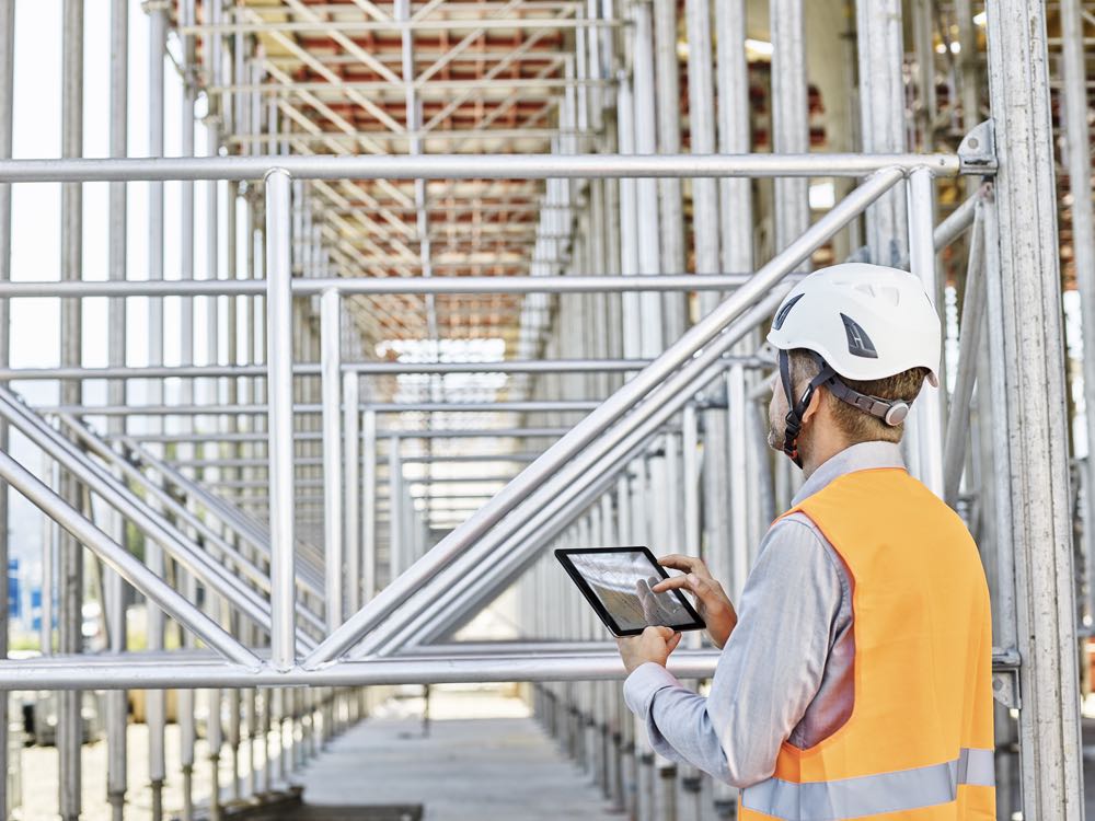 A construction worker holding a tablet and looking at the construction in progress.